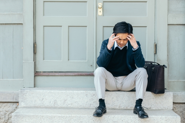 扉の前に座り込み頭を抱える男性の画像
