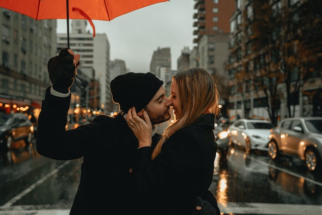 雨の中傘を差しながら顔を寄せ合うカップルの画像