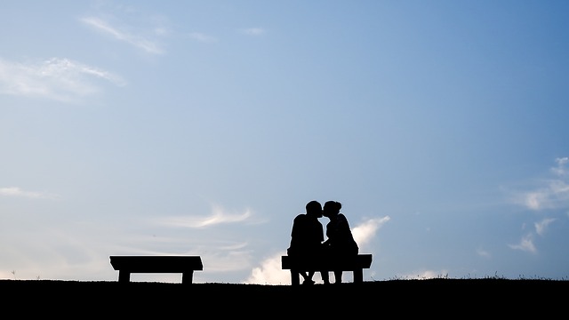 青空を背景に男女がベンチに座ってキスしている画像