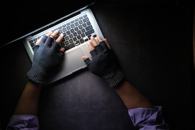 黒の手袋をはめた手がパソコンを触っている画像